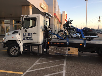 A motorcycle on the back of a flatbed truck with Lulus Wrecker logo on gate